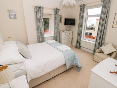 A bedroom with a double bed bedside tables a chest of drawers a chair and windows with curtains at The Headlands - Gower in The Mumbles