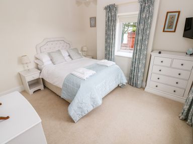 A bedroom with a double bed nightstand chest of drawers window with curtains at The Headlands - Gower in The Mumbles