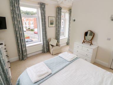 A bedroom with two windows blue floral curtains an armchair a white dresser with a mirror and a bed with folded towels at The Headlands - Gower in The Mumbles