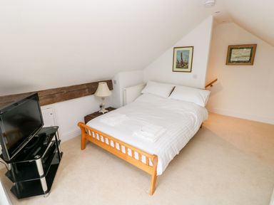 A bedroom with a double bed a wooden bed frame a TV on a glass stand and framed pictures on the walls at The Headlands - Gower in The Mumbles