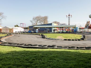An outdoor go-kart track with tires along the edges and amusement park rides in the background at Number 8 Lakes View Brean