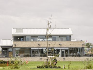 A modern two-story building with large glass windows a white roof and outdoor seating at Number 8 Lakes View in Brean