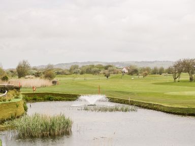 A golf course with a water hazard and fountain with hills in the background at Number 8 Lakes View in Brean