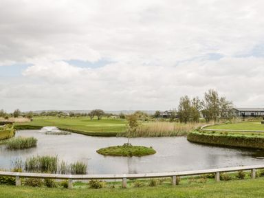 A view of a golf course with a pond and trees near Number 8 Lakes View in Brean