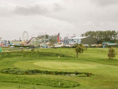 A golf green with a flag and an amusement park with rides and ferris wheel in the background at Number 8 Lakes View in Brean