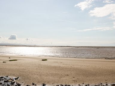 A sandy beach with patches of grass and water under a clear sky at Number 8 Lakes View in Brean