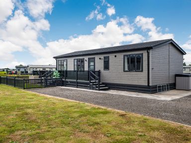 A single-story modular home with a fenced yard and steps leading to a glass-panelled porch at Number 8 Lakes View in Brean