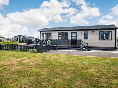 An external view of a single-story modern mobile home with a fenced yard at Number 8 Lakes View in Brean
