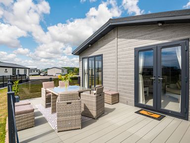 An outdoor patio with a dining table and chairs beside a modern cabin at Number 8 Lakes View in Brean