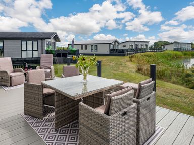 An outdoor patio with wicker chairs and a table with flowers near a lake at Number 8 Lakes View in Brean