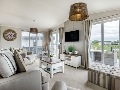 A living room with sofas a coffee table a wall clock and a television at Number 8 Lakes View in Brean