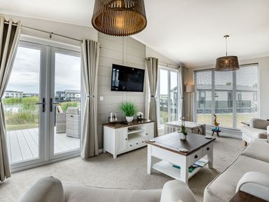 A living room with sofas a coffee table a TV on the wall and large windows at Number 8 Lakes View in Brean