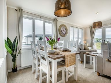 A dining area with a table set with bowls and glasses next to a living room with sofas and side tables at Number 8 Lakes View in Brean