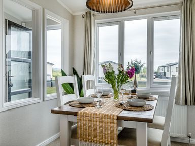 A dining area with a wooden table set with bowls and glasses and flowers on the table at Number 8 Lakes View in Brean