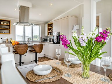 A kitchen and dining area with a wooden table set with bowls glasses and flowers at Number 8 Lakes View in Brean