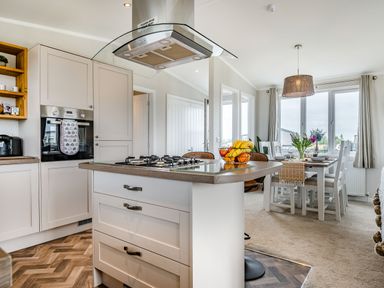 A kitchen with an island and gas stove next to a dining area with a table set for four at Number 8 Lakes View in Brean