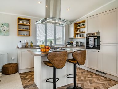 A kitchen with a countertop island with two bar stools and fruit bowl at Number 8 Lakes View in Brean