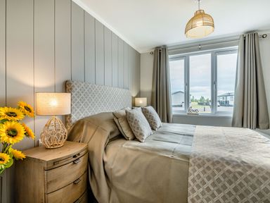 A bedroom with a bed bedside tables lamps sunflowers and curtains by the window at Number 8 Lakes View in Brean