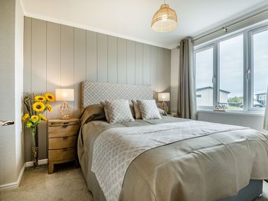 A bedroom with a bed two bedside tables lamps and sunflowers near the window at Number 8 Lakes View in Brean