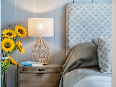 A bedside table with a lamp, book, sunflowers next to a bed with patterned headboard and pillows at Number 8 Lakes View in Brean