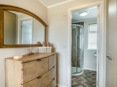 A dresser with a mirror and a basket with towels next to an entrance to a bathroom with a shower at Number 8 Lakes View in Brean