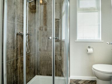 A bathroom with a glass shower enclosure a window with blinds and a toilet at Number 8 Lakes View in Brean