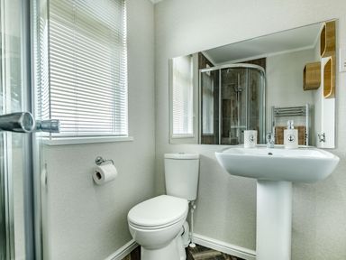 A bathroom with a toilet sink mirror window with blinds and shower at Number 8 Lakes View in Brean