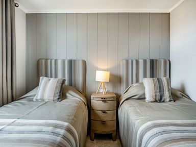 A bedroom with two single beds a bedside table with a lamp and striped cushions at Number 8 Lakes View in Brean