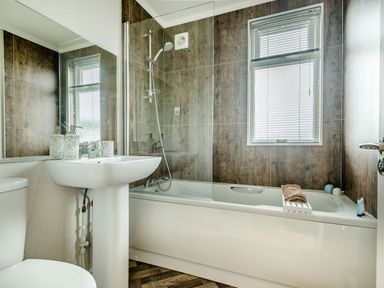 A bathroom with a white bathtub a shower sink toilet and a window at Number 8 Lakes View in Brean