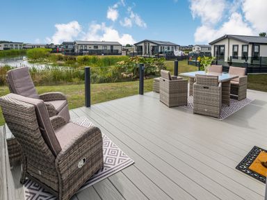 A patio with outdoor wicker chairs and table overlooking a pond and multiple modern homes at Number 8 Lakes View in Brean