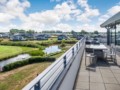 An outdoor terrace with tables and chairs overlooking a pond and several small houses at Number 8 Lakes View in Brean