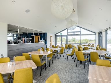 A dining area with tables and yellow chairs and a bar counter at Number 8 Lakes View in Brean