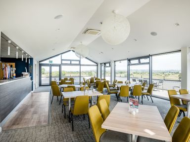 A dining area with tables and yellow chairs next to large windows and a bar at Number 8 Lakes View in Brean