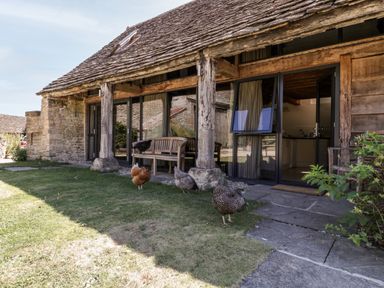 A stone and wood cottage exterior with glass doors and chickens on the grass at Tinkley Cottage in Nympsfield near Nailsworth