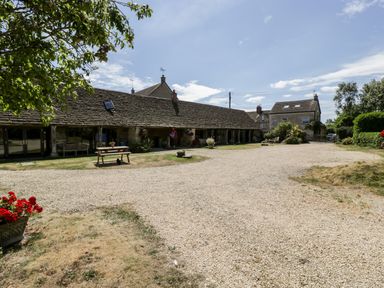 A courtyard with a gravel driveway benches and potted plants outside stone cottages at Tinkley Cottage in Nympsfield near Nailsworth