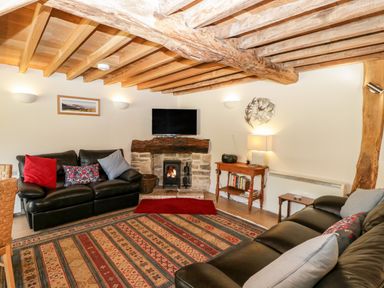 A living room with leather sofas a stone fireplace with a wood burner a wooden beamed ceiling and a patterned rug at Tinkley Cottage in Nympsfield near Nailsworth