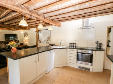 A kitchen with white cabinets black countertops a built in oven a sink and a kettle at Tinkley Cottage in Nympsfield near Nailsworth