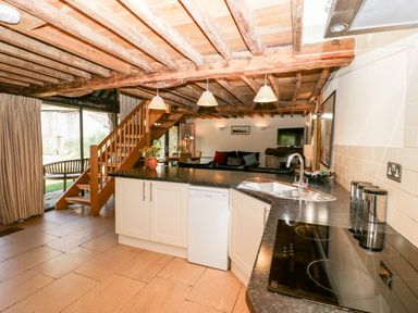 An open kitchen and living area with wooden beams a staircase and a sofa at Tinkley Cottage in Nympsfield near Nailsworth