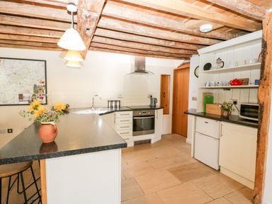 A kitchen with a black countertop island with flowers a stove white cabinets and wooden beams on the ceiling at Tinkley Cottage in Nympsfield near Nailsworth