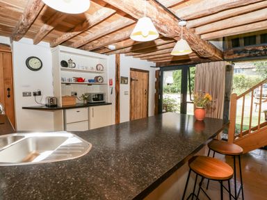 A kitchen with wooden beams stools and a sink with a window door showing the outside at Tinkley Cottage in Nympsfield near Nailsworth