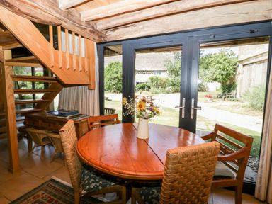 A dining area with a round wooden table and mixed chairs near glass doors overlooking a garden at Tinkley Cottage in Nympsfield near Nailsworth