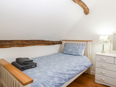 A bedroom with a single bed with blue floral bedding a bedside table with drawers and a lamp at Tinkley Cottage in Nympsfield near Nailsworth