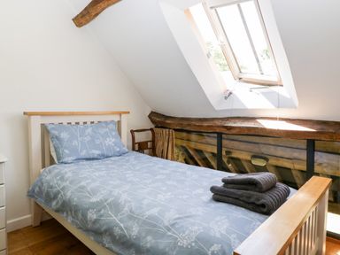 A bedroom with a single bed folded towels on the bed and a skylight window at Tinkley Cottage in Nympsfield near Nailsworth