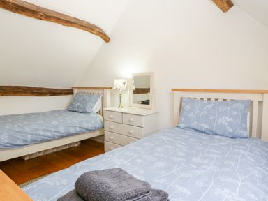 A bedroom with two single beds a chest of drawers with a lamp and mirror at Tinkley Cottage in Nympsfield near Nailsworth