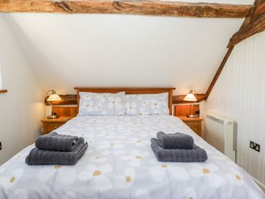 A bedroom with a double bed and two folded dark towels on the bed at Tinkley Cottage in Nympsfield near Nailsworth