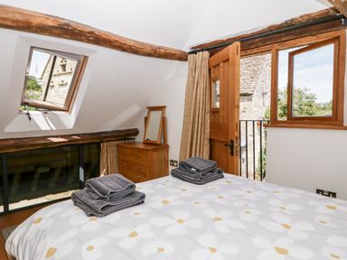 A bedroom with a bed folded towels a wooden dresser mirror open window and wooden door at Tinkley Cottage Nympsfield near Nailsworth