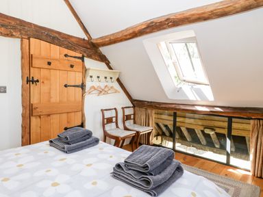 A bedroom with a wooden door two chairs folded towels on a bed and a skylight window at Tinkley Cottage in Nympsfield near Nailsworth