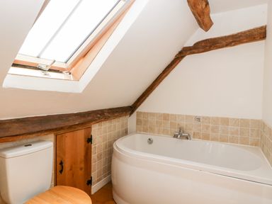 A bathroom with a bathtub a toilet a skylight window and exposed wooden beams at Tinkley Cottage in Nympsfield near Nailsworth