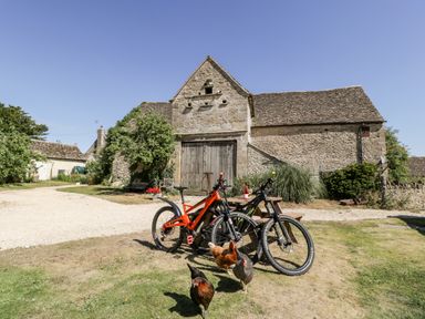 Two bicycles next to a wooden picnic table with chickens in front of a stone barn at Tinkley Cottage in Nympsfield near Nailsworth