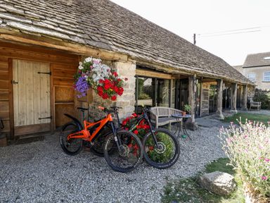 Two bicycles parked outside a stone cottage with wooden doors and hanging flower baskets at Tinkley Cottage in Nympsfield near Nailsworth